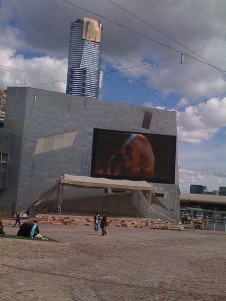 Federation Square, Melbourne: giant screen on sandstone building, people strolling across the paving