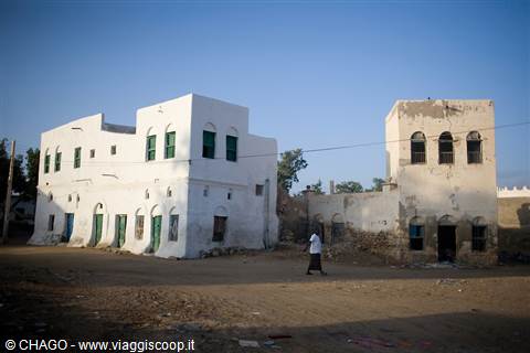Man walks past white coral-block houses in Massawa under clear sky