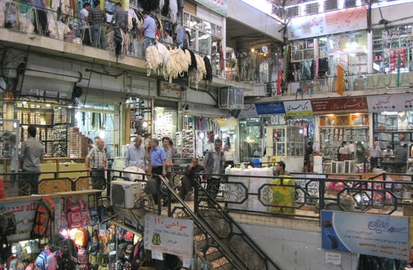 Two-story covered bazaar, clothing shops and shoppers among Persian signs