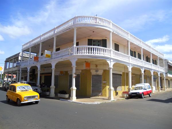 Yellow car passing a white colonial building with double corner arcade