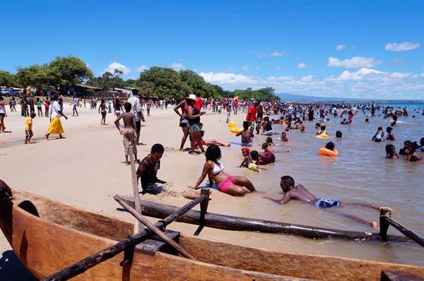 Swimmers on the sand beside a wooden dugout canoe, crowded sunny beach