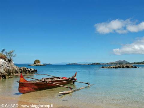 Wooden outrigger canoe beached on shore, turquoise water and islets