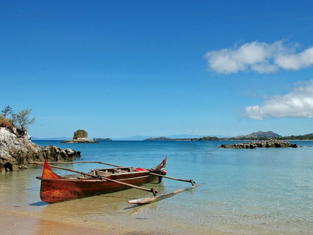 Piroga in legno con bilanciere arenata sulla spiaggia, acque turchesi e isole