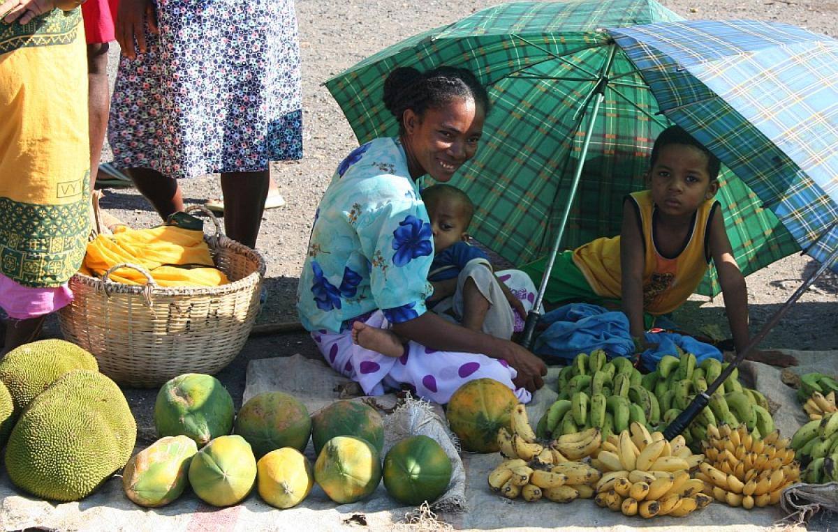 Donna e bambini vendono banane, papaya e jackfruit sotto un ombrellone verde al mercato