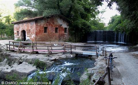 Old red stone mill beside a small waterfall and wooden footbridge