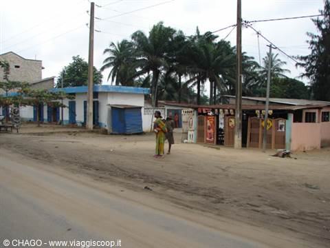 Woman with child on dirt road in front of small shops and palm trees