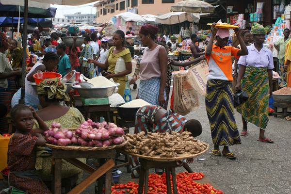 Bustling market: women selling onions, tomatoes and tubers on wooden tables