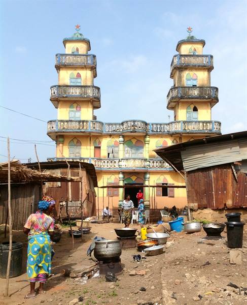 Women with cooking pots in front of yellow mosque with two concrete minarets