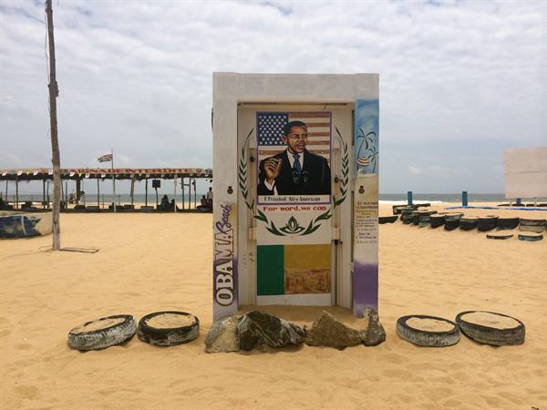 Painted door with Obama portrait on sandy beach, tires and poles around