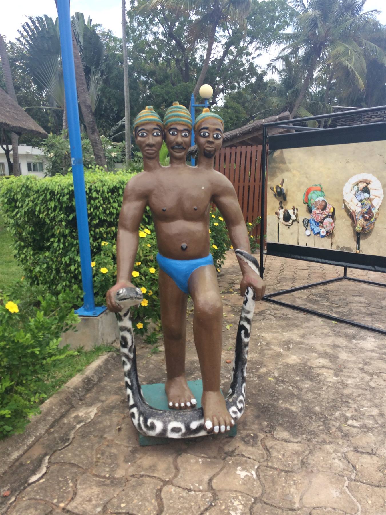 Statua a tre teste con pantofole su serpente dipinto, giardino tropicale