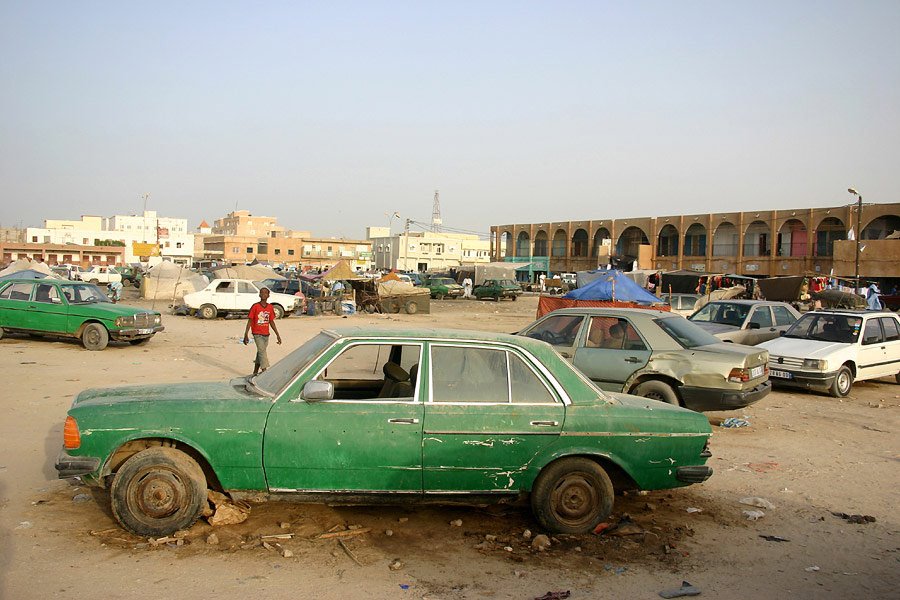 Auto d'epoca verde abbandonata sulla sabbia, mercato di una città sahariana