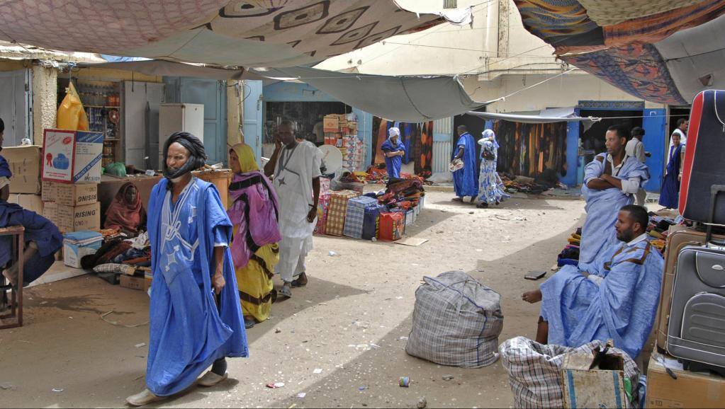 Mercato coperto con teli colorati, uomini in boubou blu e valigie in vendita