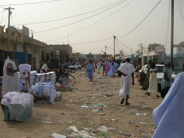 Sandy street market, men in white robes, stalls selling colorful fabrics