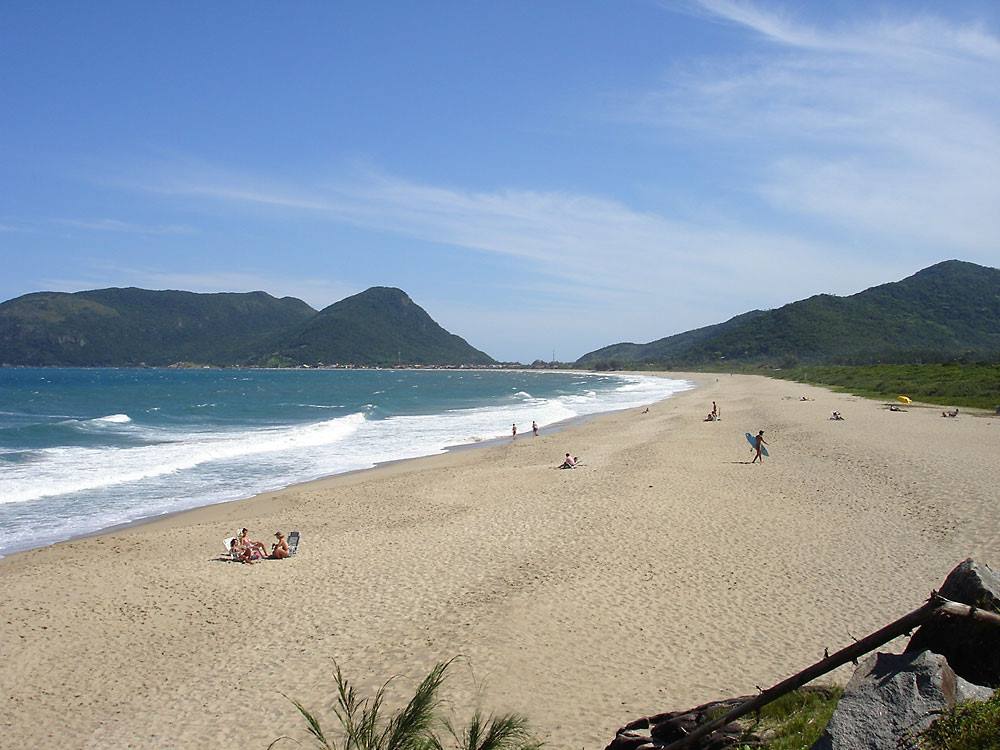 Spiaggia di sabbia con bagnanti, onde e montagne verdi sotto cielo azzurro