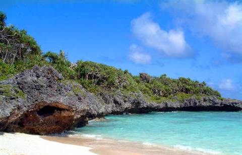 White sand beach with coral rocks, turquoise water under a blue sky