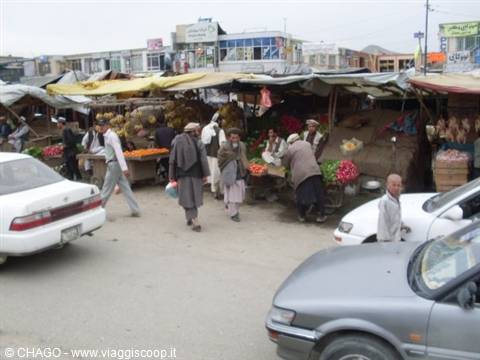 Street market with fruit stalls, men in shalwar kameez and passing cars