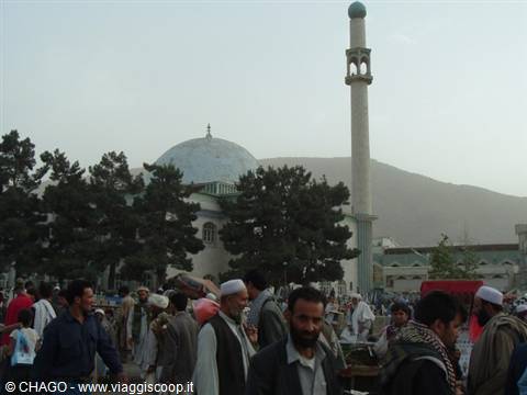 Crowd of men in front of a mosque with green dome and minaret, Kabul