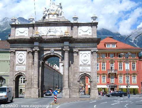 Stone triumphal arch in Innsbruck, statues on top, buildings and snowy Alps