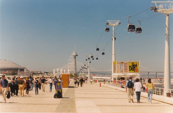 Visitors stroll beneath cable cars at Expo 98, Vasco da Gama tower behind