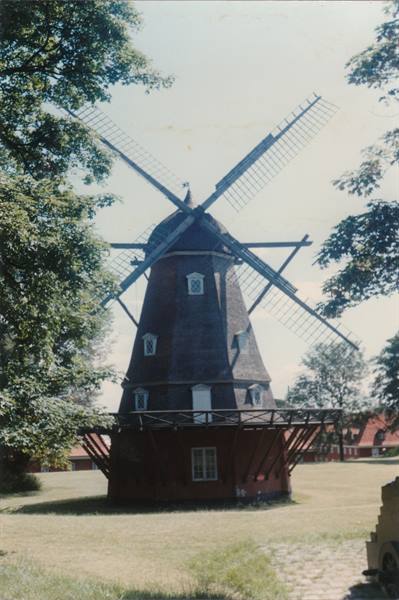 Old dark wooden windmill with large sails, surrounded by trees and grass