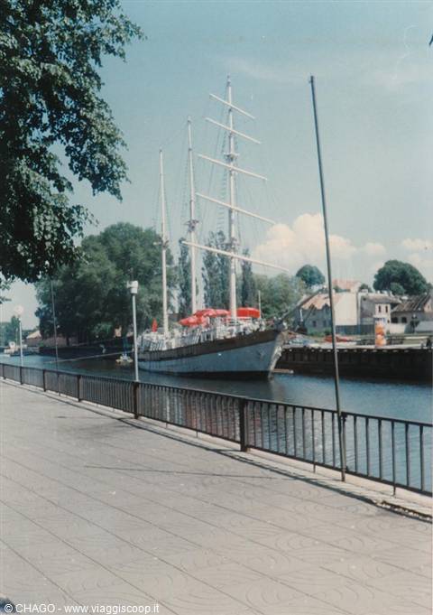 Three-masted tall ship moored by a paved quay with iron railing