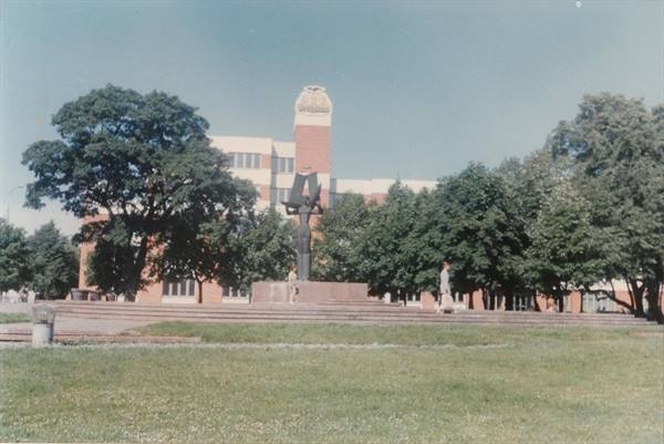 stone monument in front of a brick building among green trees