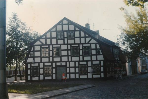 Half-timbered house with white plaster on cobblestone street, child walking by