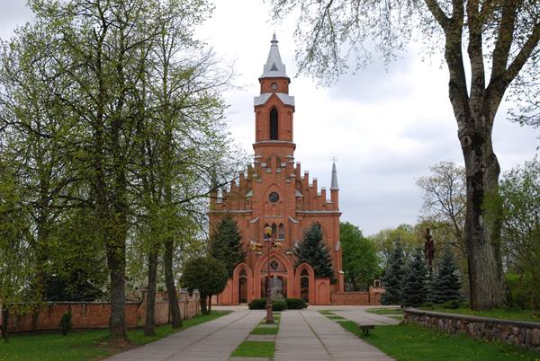 Red brick church with tall tower among green trees and paved walkway