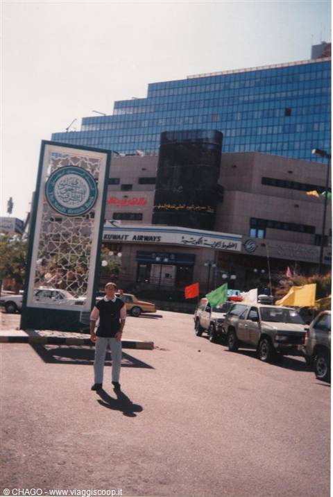 Man posing in front of Kuwait Airways agency with glass skyscraper behind