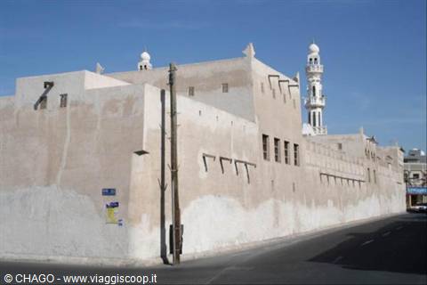 Old mud-brick building with white minaret along the street, Manama