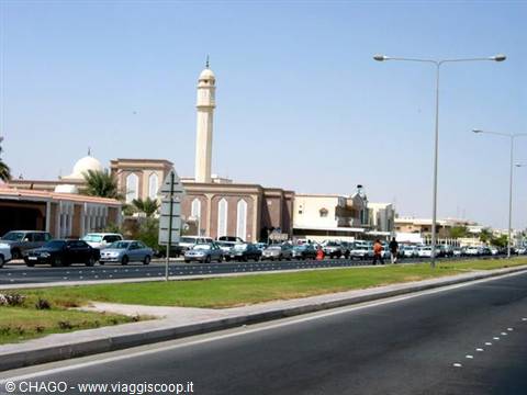 White mosque minaret beside a busy road, cars lined up under a clear sky