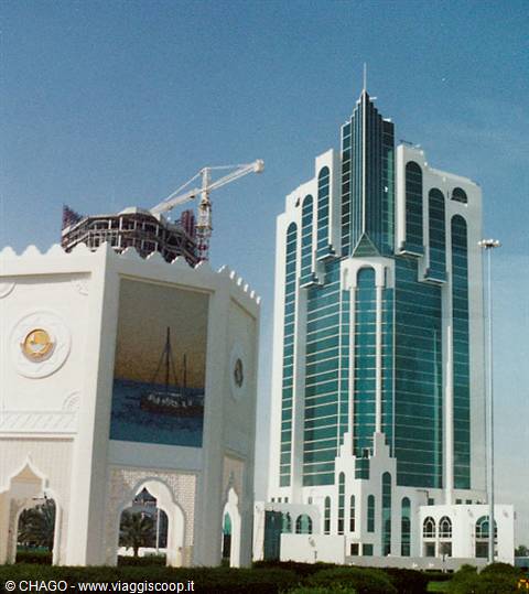 Green glass skyscraper beside white arabesque pavilion and construction site