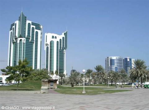 Green glass towers along Doha's corniche, palm trees and light paved promenade