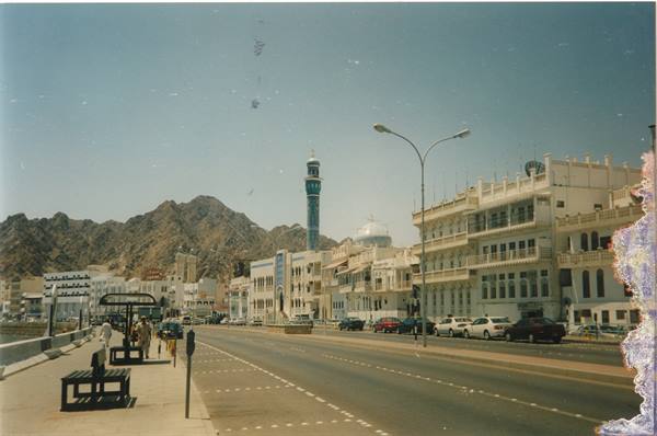 Muscat corniche: white buildings, minaret, rocky mountains and parked cars