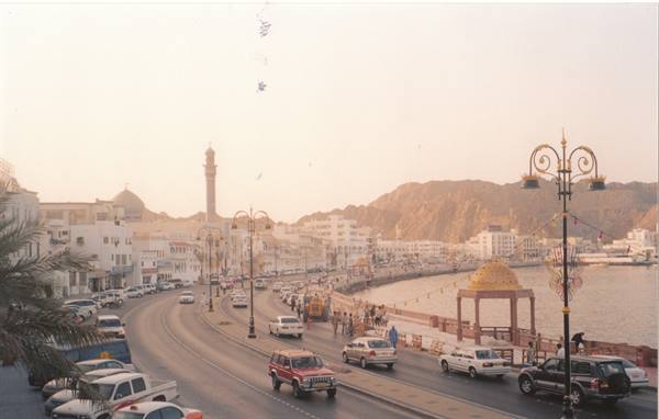 Cars driving along a seaside road, white minaret and arid mountains in Muscat