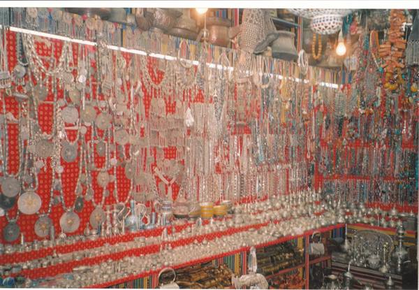Shop with silver jewelry hanging on red panels under lit lamps