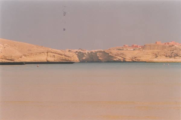 Turquoise lagoon between sandy cliffs, buildings in the distance, faded analog photo