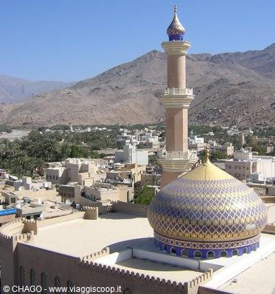 Mosque with blue and gold tiled dome and minaret, arid mountains behind, Nizwa