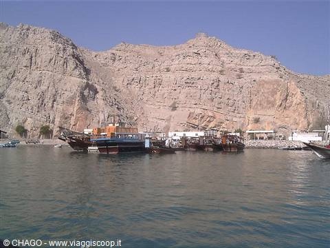 Wooden boats moored at Musandam harbor beneath arid rocky cliffs