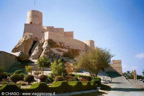 Nakhal Fort, stone and clay walls on rock, gardens and trees under blue sky