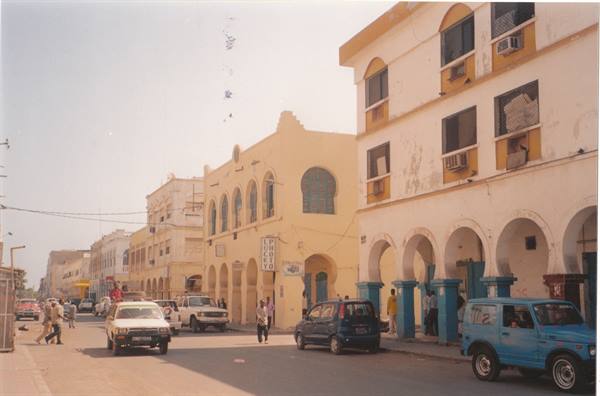 Street with traffic among yellow colonial buildings with arches, bright light