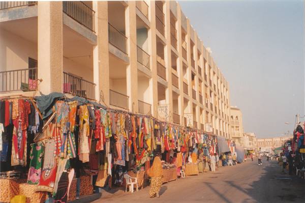Colorful fabric market under a residential building, woman in yellow walking