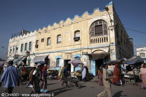 Busy market in front of a yellow colonial building with balcony and blue trim