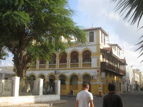 Yellow colonial building with arches and wooden balconies in Stone Town, people walking under trees