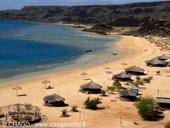 Golden sand beach with thatched parasols, boats and arid cliffs
