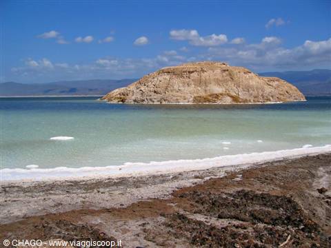 Rocky islet rising over turquoise water and white salt shoreline
