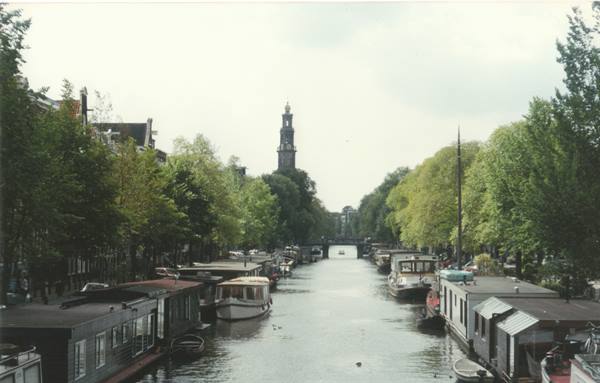 Amsterdam canal with moored houseboats and the Westerkerk tower among trees
