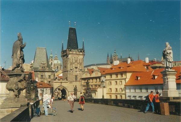 Tourists walk on Charles Bridge among stone statues and gothic tower, Prague