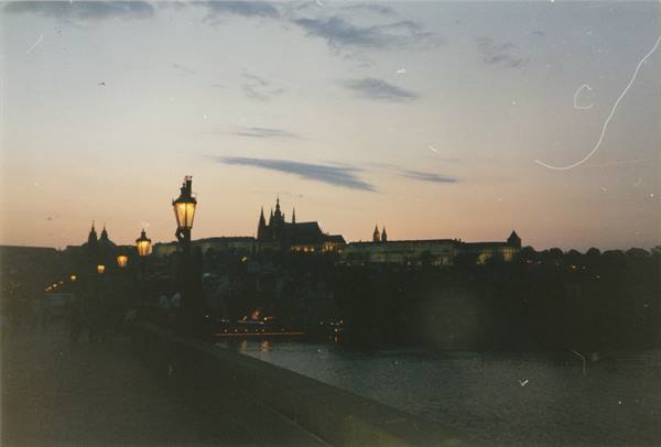 Lit streetlamp on Charles Bridge, Prague Castle at dusk