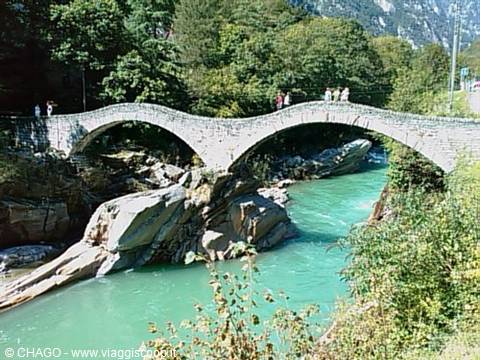 Tourists cross the Ponte dei Salti at Lavertezzo, stone arch over the turquoise Verzasca river